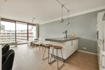 a kitchen and dining area in a condo apartment with wood floors, white walls, grey counter tops and large windows