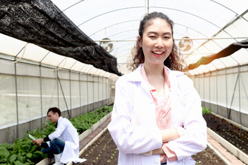 Portrait of smiling beautiful Asian botanist scientist woman in white lab coat standing with arms...