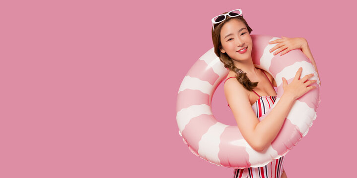 Summer holiday happy young asian woman portrait Happy young woman wear swimsuit hold pink swim ring or inflatable tube ring Lady smile and loook at camera isolated on pink color background studio shot