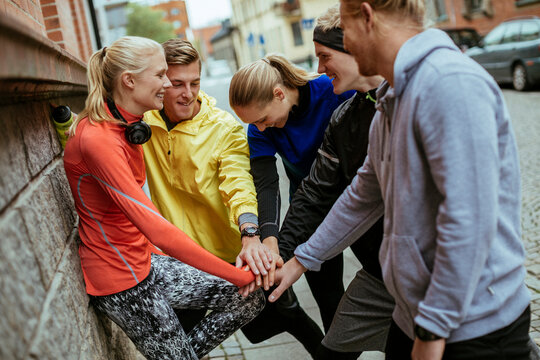 Young a diverse group of friends showing teamwork and stacking hands together while getting ready to run in the city
