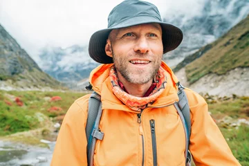 Photo sur Plexiglas Makalu Portrait of smiling Man with backpack dressed orange waterproof jacket and funny hat walking the path during Makalu Barun National Park trek in Nepal. Mountain hiking and active people concept image.
