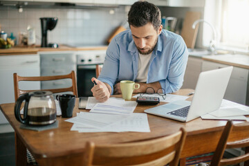 Stressed young man going over bills and payments in the kitchen