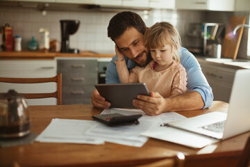 Young father using the tablet with his daughter in the kitchen