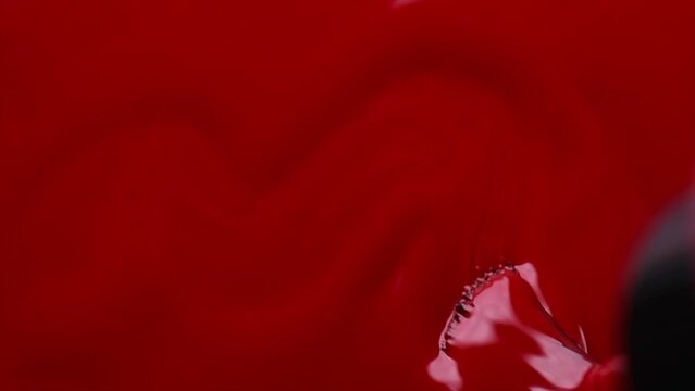 Nail polish liquid surface, red shellac UV gel brush, varnish, manicure concept, slow motion. Manicure salon, shellac texture background, backdrop. Top view