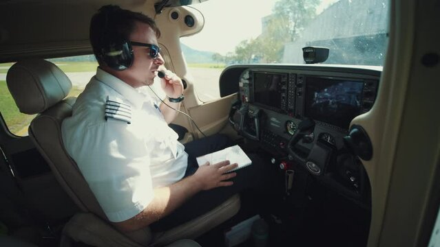 The pilot in the airplane cabin communicates with the control tower, wearing headset, preparing for a flight