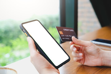 A female hands holding a smartphone white screen mockup and a credit card over blurred background. online shopping, credit card payment, mobile banking.