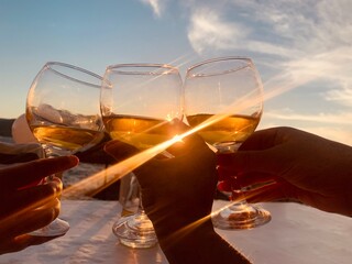 A group of friends raise a toast with glasses of white wine, sunset . 