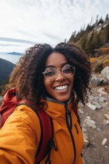 Fototapeta na wymiar Woman with glasses takes selfie on top of mountain and smiles, happy woman