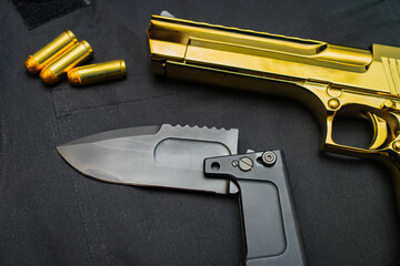 Firearms and bladed weapons. Gold color Desert Eagle pistol and folding tactical knife, close up.