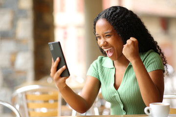 Excited black woman checking smart phone in a bar