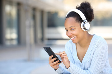 Happy black woman using headphone and phone posing
