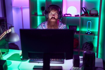 Young redhead man streamer playing video game using computer at gaming room