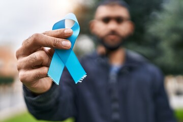 Young hispanic man holding light blue ribbon at park
