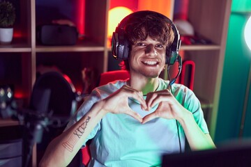 Young blond man streamer smiling confident doing heart symbol with hands at gaming room