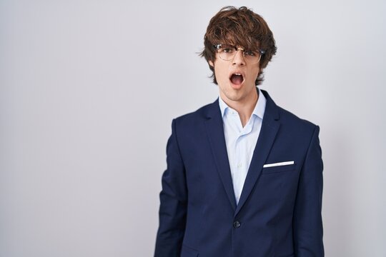 Hispanic business young man wearing glasses in shock face, looking skeptical and sarcastic, surprised with open mouth