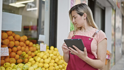 Young blonde woman shop assistant using touchpad working at fruit store