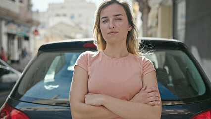 Young blonde woman standing by car with arms crossed gesture at street