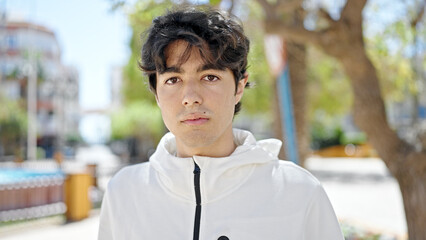 Young hispanic man standing with serious expression at park
