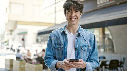 Young hispanic man using smartphone smiling at coffee shop terrace