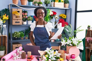 African american woman florist smiling confident using laptop at florist store