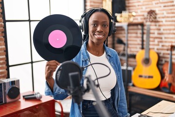 Beautiful black woman holding vinyl record at music studio looking positive and happy standing and smiling with a confident smile showing teeth