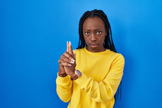 Beautiful black woman standing over blue background holding symbolic gun with hand gesture, playing killing shooting weapons, angry face