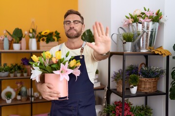 Middle age man with beard working at florist shop holding plant with open hand doing stop sign with serious and confident expression, defense gesture