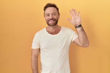 Fototapeta premium Middle age man with beard standing over yellow background showing and pointing up with fingers number five while smiling confident and happy.