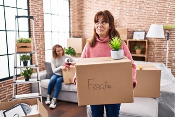 Mother and daughter moving to a new home holding cardboard box smiling looking to the side and...