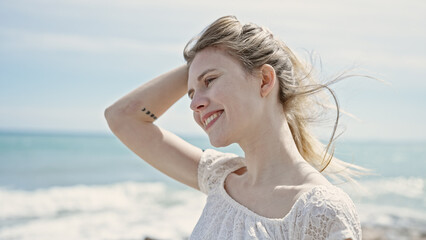 Fototapeta na wymiar Young blonde woman tourist smiling confident touching hair at beach