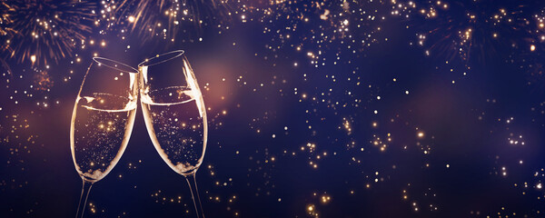 two toasting champagne flutes on glittering fireworks night sky with blurred lights and copy space for greetings, happy new year concept