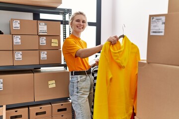 Young blonde woman ecommerce business worker organizing clothes on coat rack at office