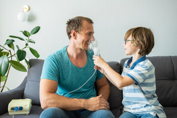 Funny child boy helps his father to do nebulizer inhalation. How to teach children not to be afraid of medical treatment - obrazy, fototapety, plakaty