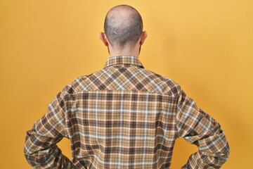 Young hispanic man with tattoos standing over yellow background standing backwards looking away with arms on body