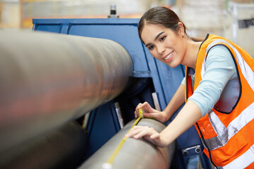 female factory worker using tape measure and measuring the length of the steel pipe in the factory