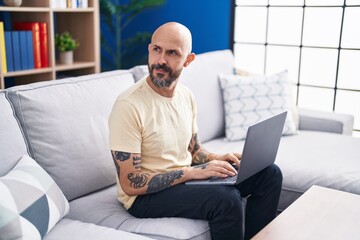 Young bald man using laptop sitting on sofa at home