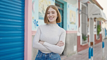 Young blonde woman standing with crossed arms at street