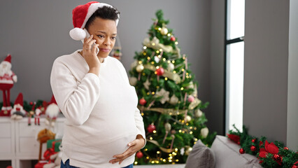 Obraz na płótnie Canvas Young pregnant woman celebrating christmas talking on smartphone at home