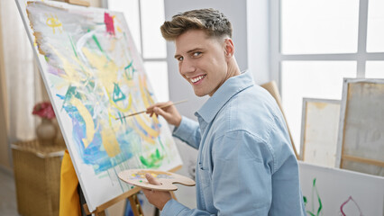 Smiling young caucasian artist confidently drawing in an indoor art studio, enjoying the joy of creativity