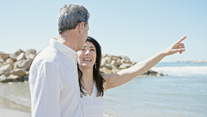 Senior man and woman couple smiling confident pointing with finger to side at seaside