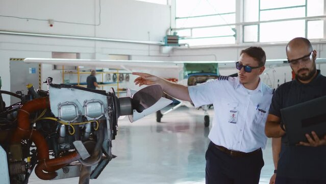 Pilot and aircraft maintenance mechanic checking airplane in airport hangar using laptop