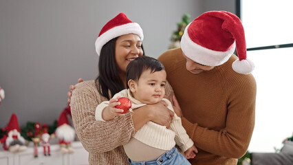 Couple and son holding decoration ball standing by christmas tree at home