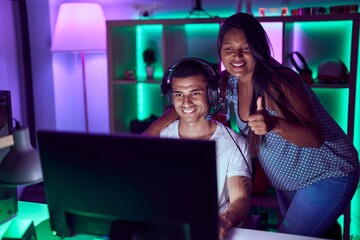 Young hispanic couple playing video games smiling happy and positive, thumb up doing excellent and approval sign