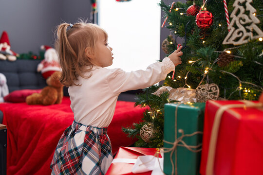 Adorable blonde girl decorating christmas tree at home