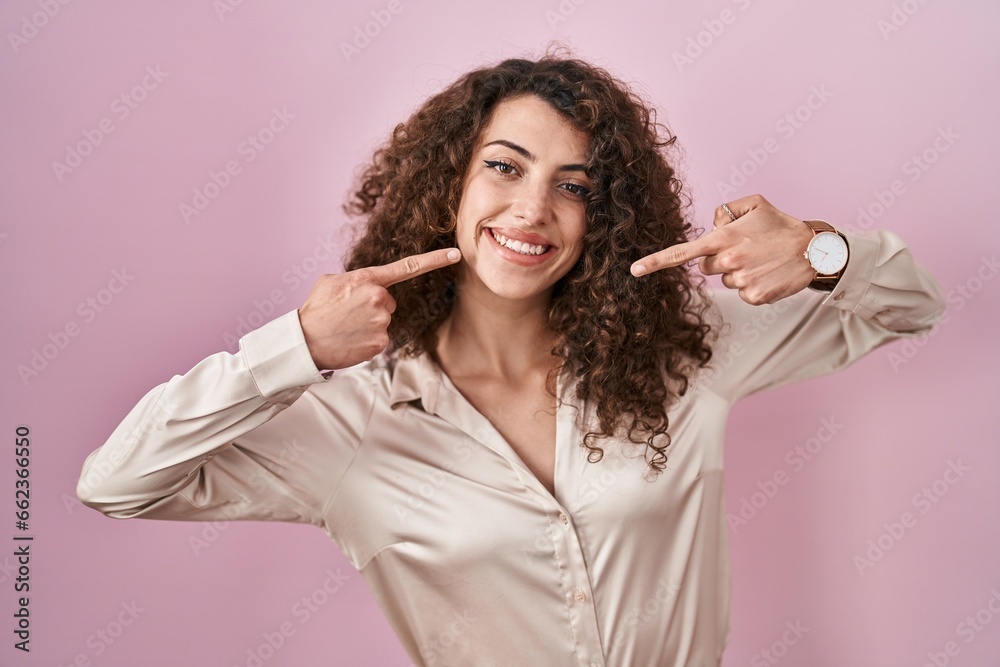 Sticker hispanic woman with curly hair standing over pink background smiling cheerful showing and pointing w