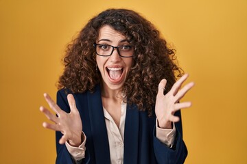 Hispanic woman with curly hair standing over yellow background celebrating crazy and amazed for success with arms raised and open eyes screaming excited. winner concept