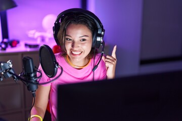 Hispanic young woman playing video games smiling with an idea or question pointing finger with happy face, number one