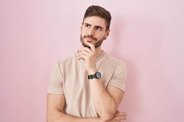 Hispanic man with beard standing over pink background with hand on chin thinking about question,...
