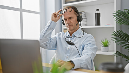 Fototapeta premium Work-weary middle age man takes off glasses after intense business video call in office