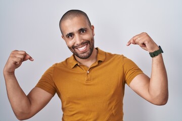 Hispanic man with beard standing over white background looking confident with smile on face,...